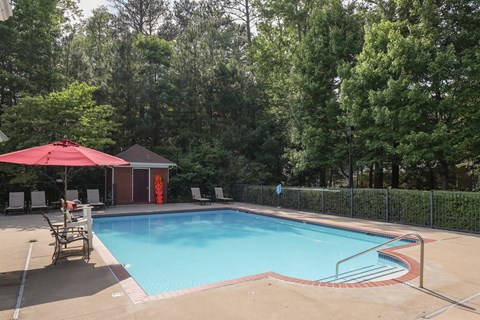 a swimming pool with a red umbrella and chairs around it