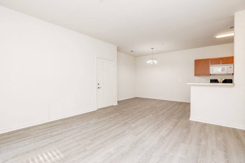an empty living room and kitchen with white walls and wood flooring