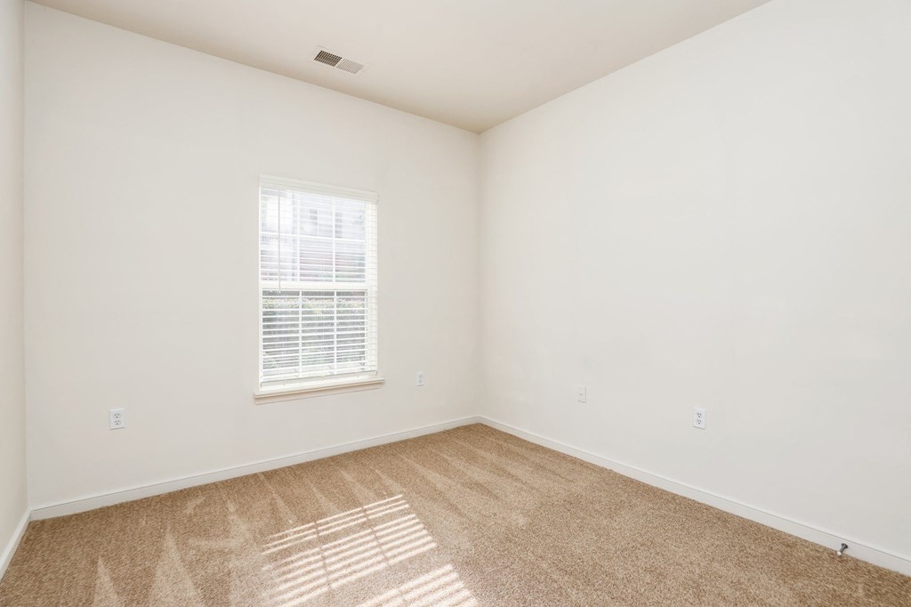a bedroom with white walls and carpet and a window