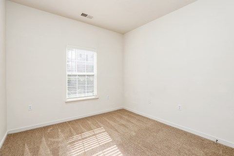 a bedroom with white walls and carpet and a window