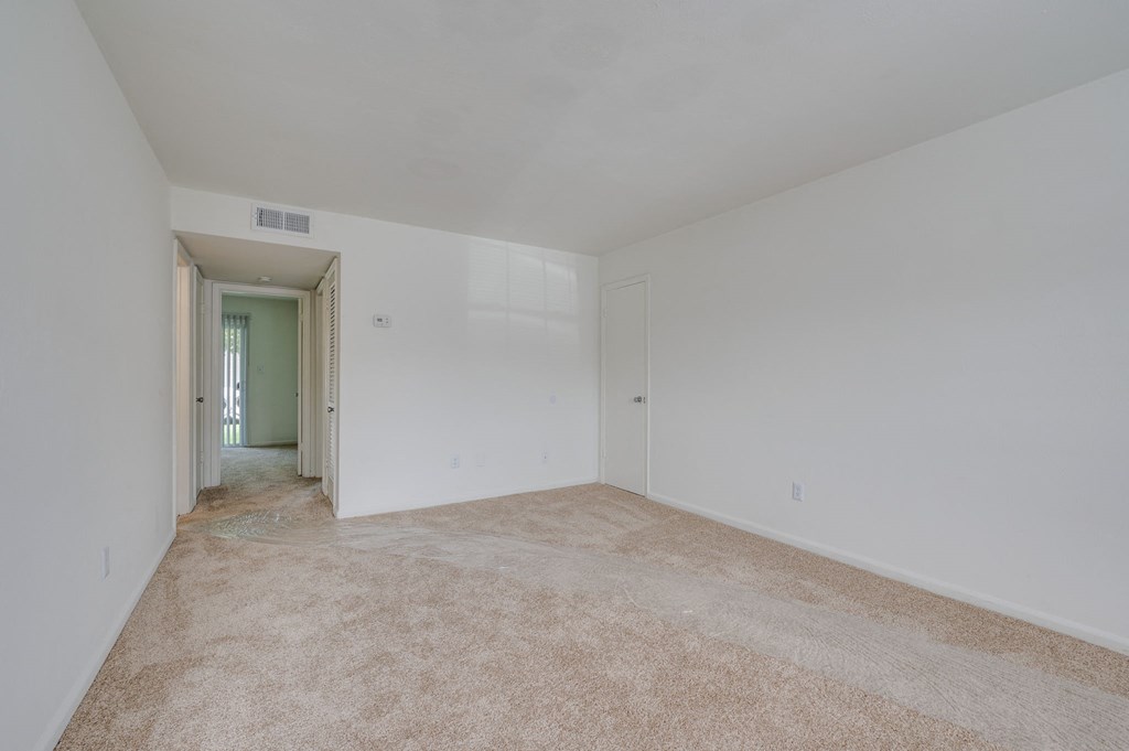 a bedroom with white walls and carpet and a door to a hallway