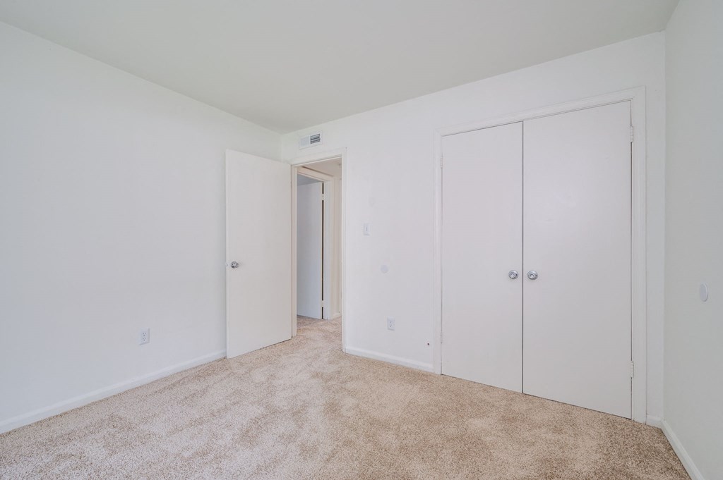 a bedroom with white walls and carpet and white closets