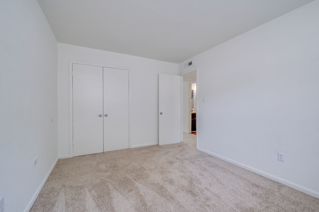a bedroom with white walls and carpet and white closets