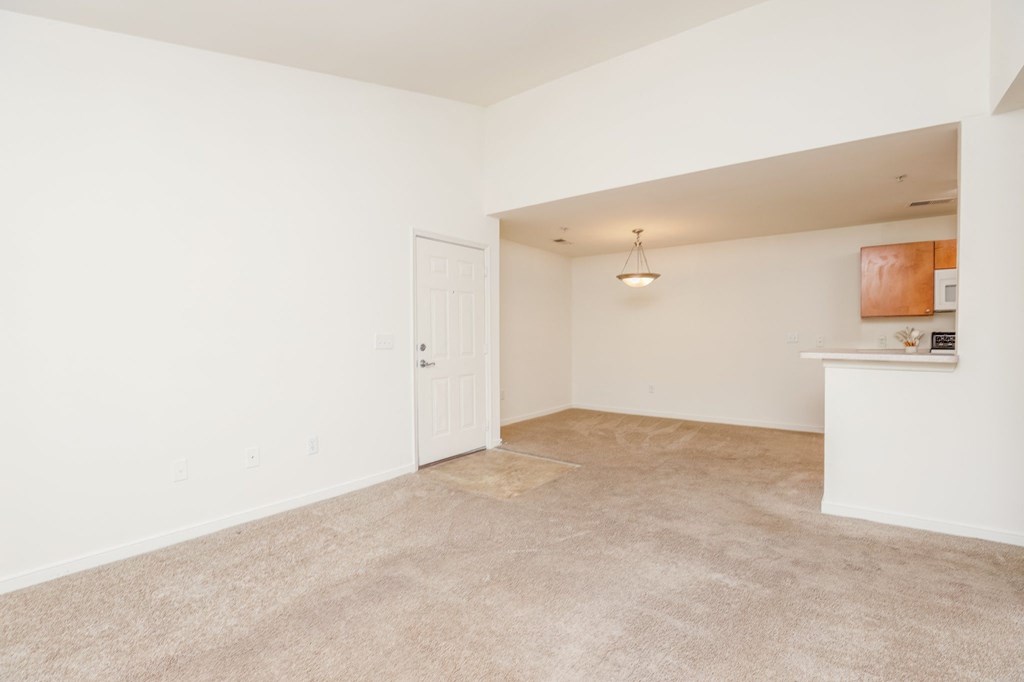 the living room and dining room of an apartment with carpeting and a white door