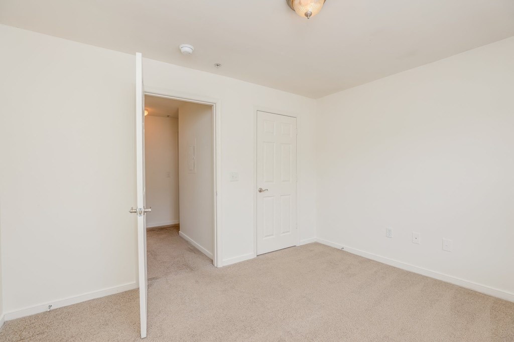 a bedroom with white walls and carpet and a door to a closet