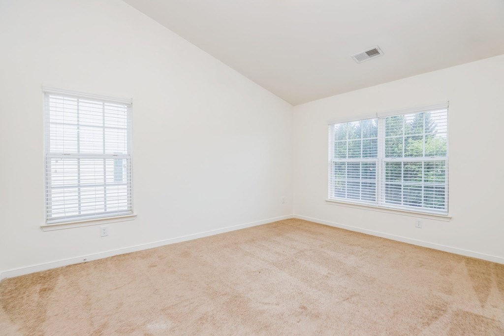 an empty bedroom with two windows and a carpeted floor
