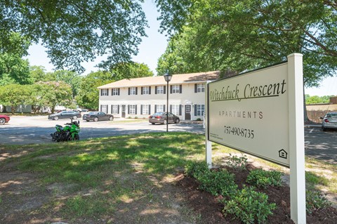 a sign in front of a building with trees and a parking lot