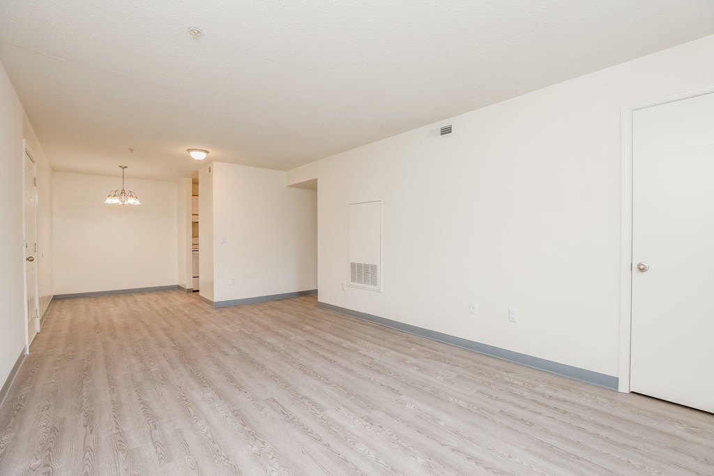a spacious living room with white walls and wood flooring