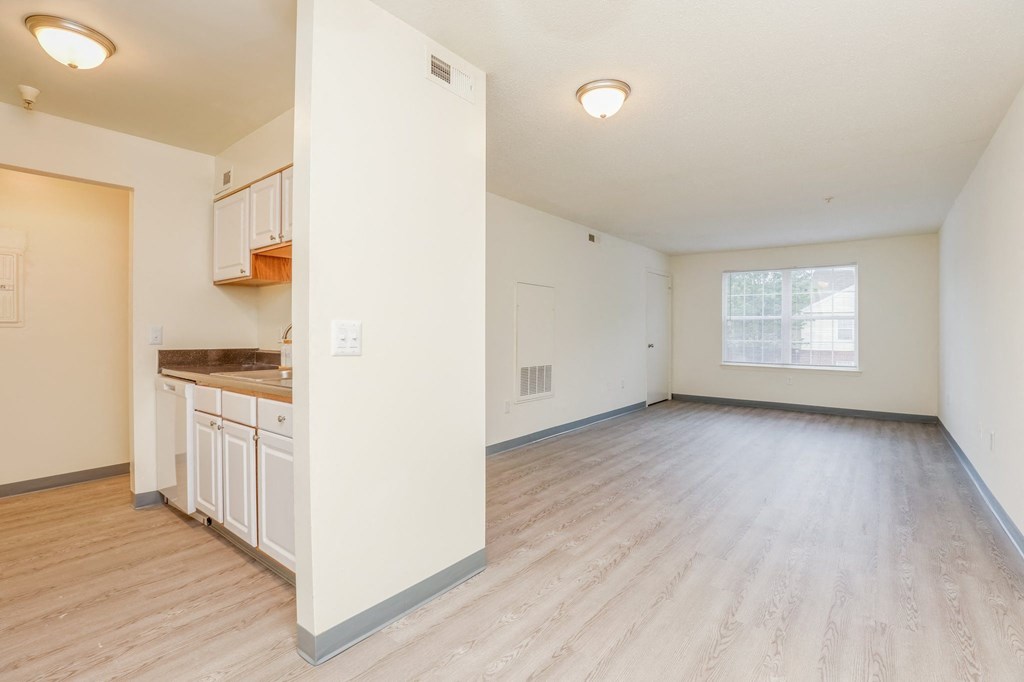 an empty living room and kitchen with wood flooring and a window