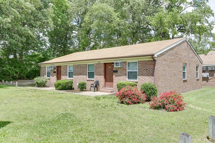 a small brick house with a lawn and trees