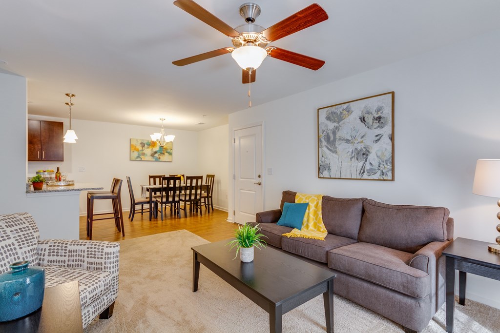 A living room with a brown couch, a blue vase, and a ceiling fan.