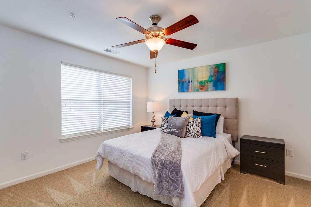 A bedroom with a bed, a ceiling fan, and a painting on the wall.