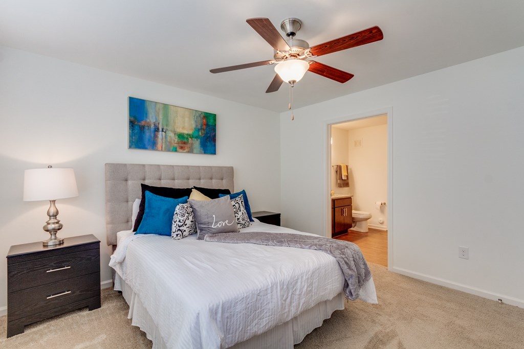 A bedroom with a bed, a ceiling fan, and a painting on the wall.