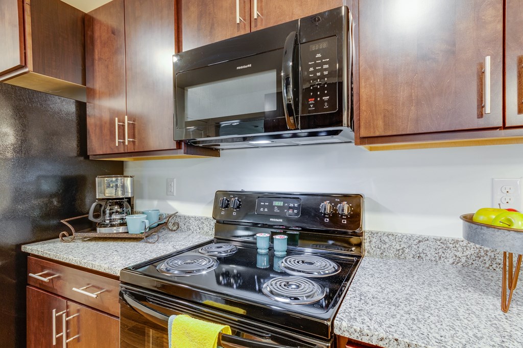 A black microwave is mounted above a stove in a kitchen.