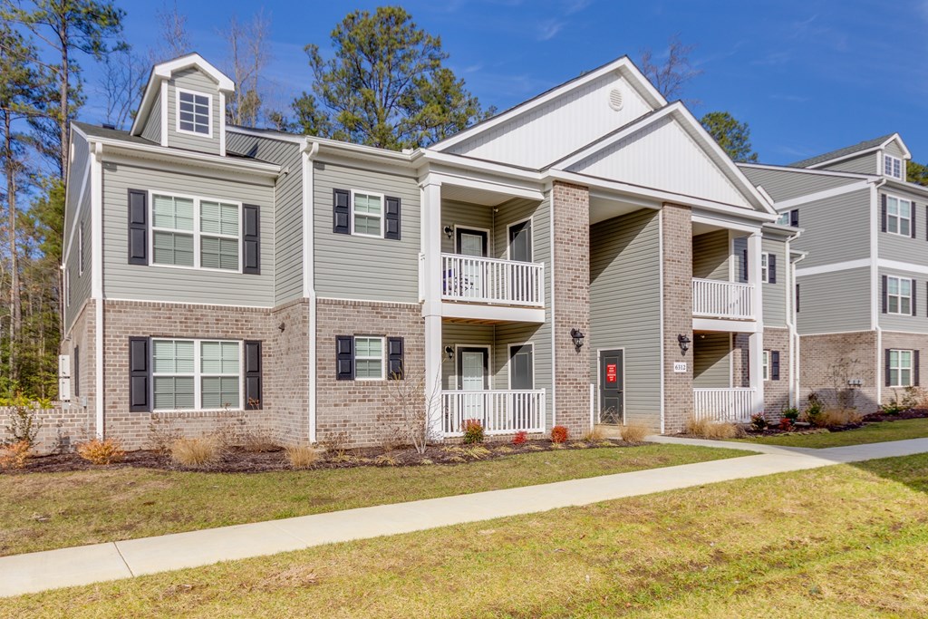A grey two story apartment building with a balcony on the second floor.