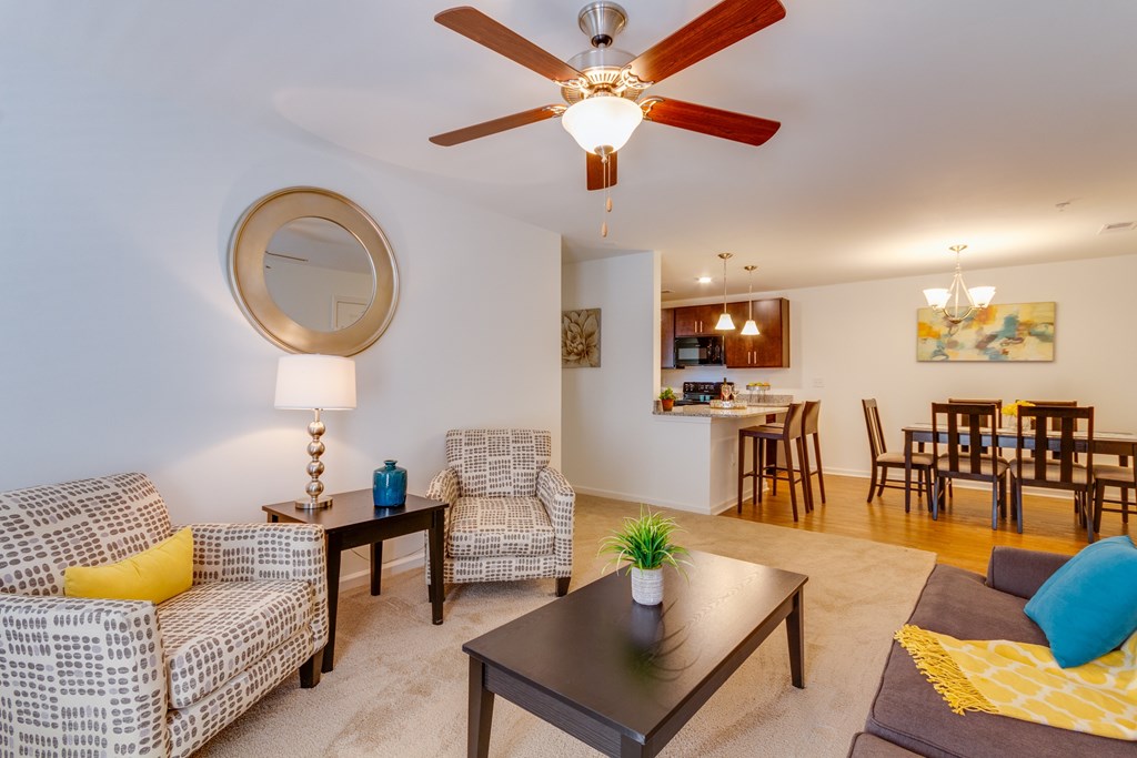 A living room with a ceiling fan and a dining area in the background.