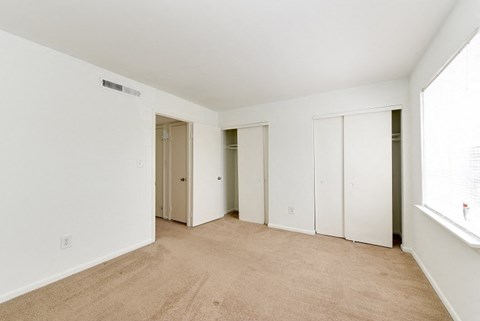 a bedroom with white walls and a carpeted floor and three closets