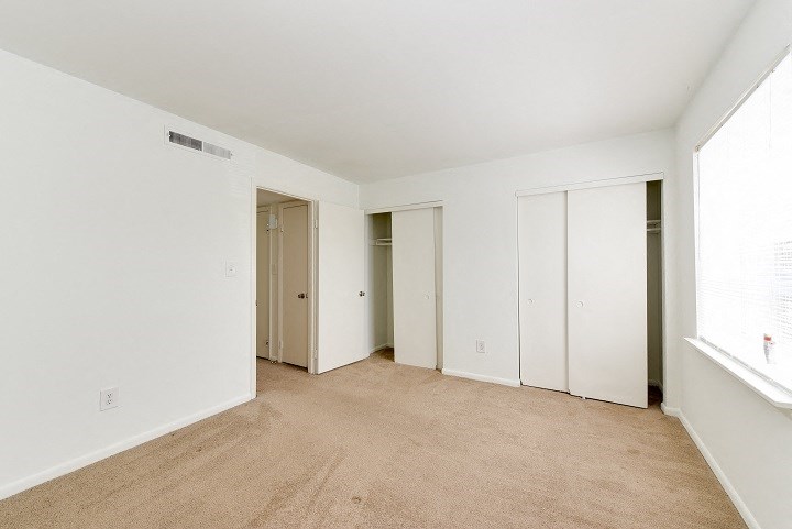 a bedroom with white walls and a carpeted floor and three closets