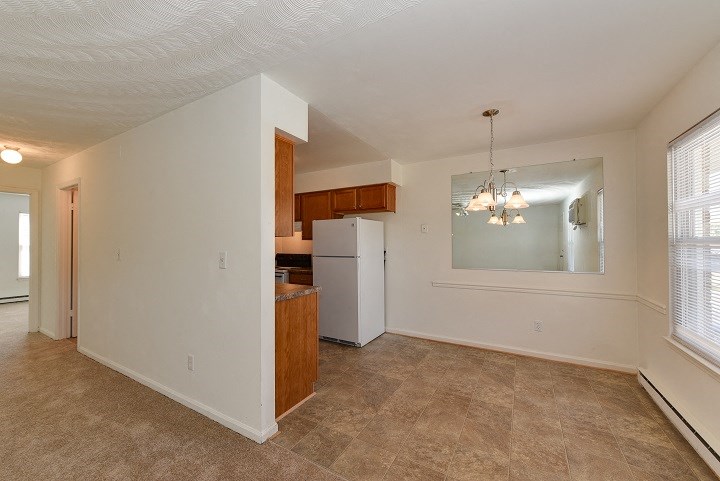 an empty living room with a kitchen with a refrigerator