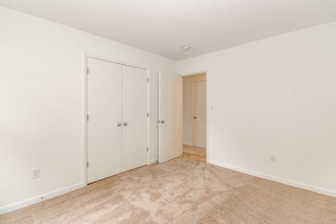 a bedroom with white walls and carpeting and closet doors