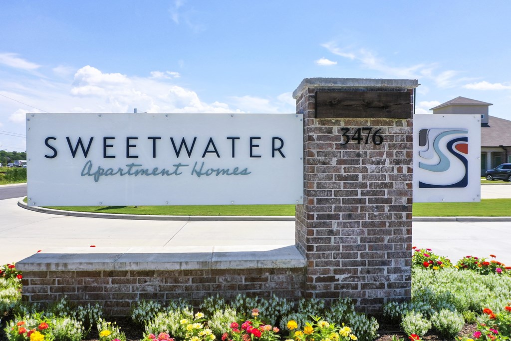 a sign for sweetwater apartment homes in front of a sidewalk and flowers