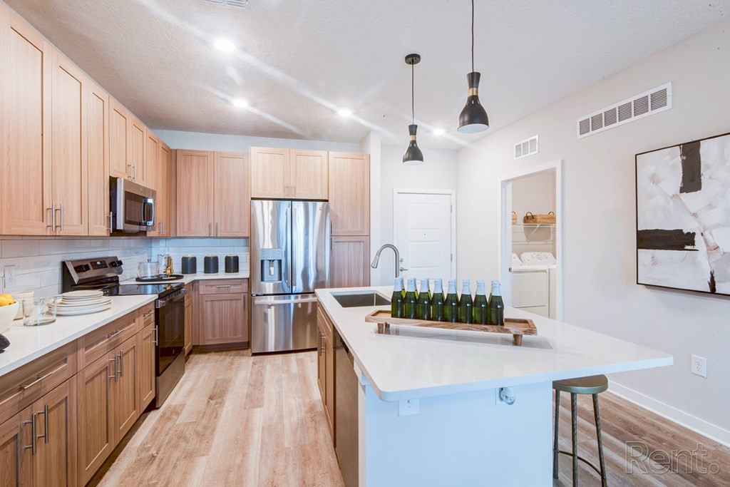 Modern kitchen with white quartz island, pendant lighting, and stainless steel appliances. A kitchen with wooden cabinets and a white quartz island at Tapestry Nona in Orlando, FL