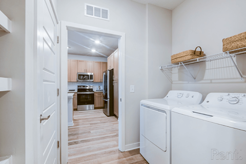 A white washing machine is in a laundry room with a doorway to a kitchen.