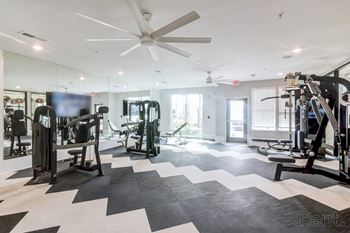 A spacious gym with a variety of equipment and a ceiling fan at Tapestry Nona Apartments in Orlando, FL