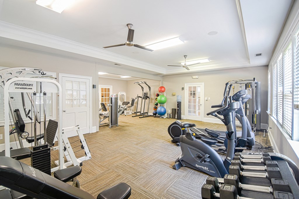 a gym with weights and other exercise equipment and windows at 10X Audubon Park apartments in Daphne, AL 