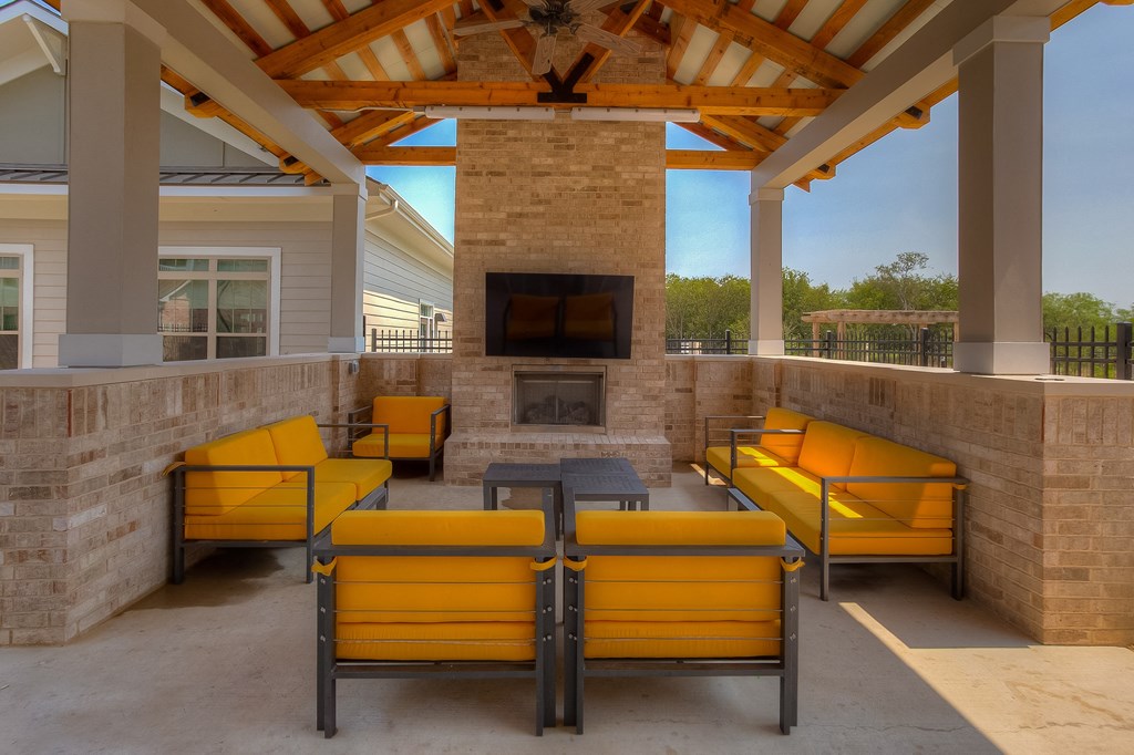 a covered patio with a fireplace and yellow couches