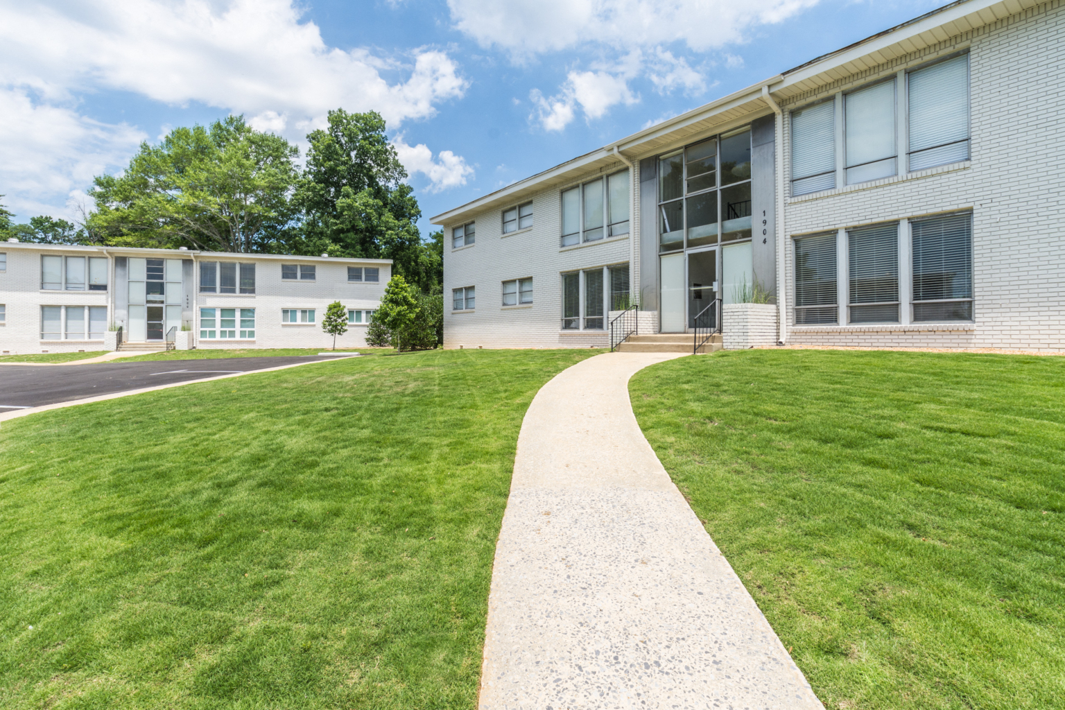 a walkway leading to an apartment building with green grass