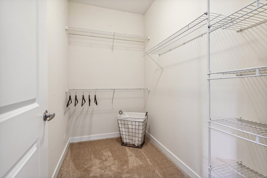 a walk in closet with white walls and shelves and a basket on the floor at Hampton Roads Crossing, Suffolk, VA