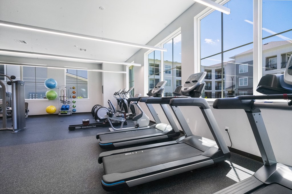 two treadmills and other exercise equipment in a gym with large windows