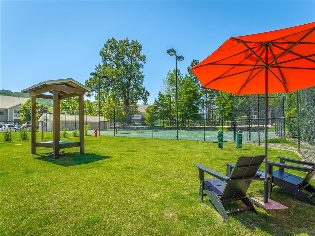 two benches and an umbrella in the grass near a tennis court