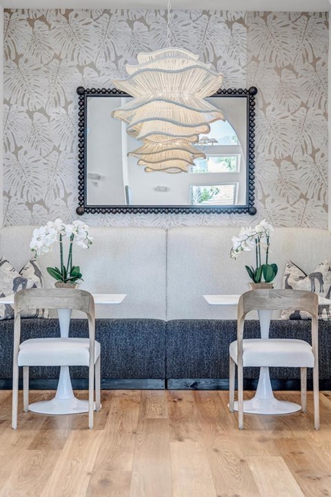 A dining room with a white table and chairs, a mirror, and a wallpapered wall.