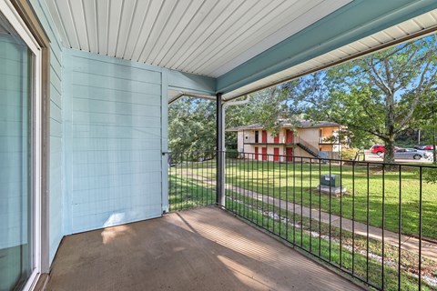 A patio with a black railing and a view of a red and white house across the way.