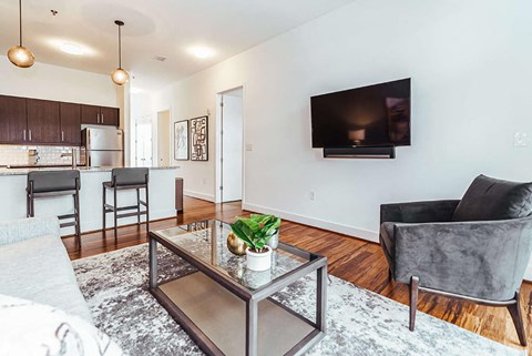 A modern living room with a grey sofa, a glass coffee table, and a flat-screen TV mounted on the wall.