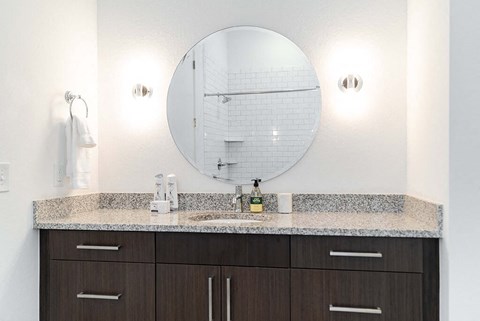 Modern bathroom vanity with granite countertop and round mirror at Reserve on 3rd Apartments, Birmingham, 35233