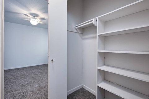 a walk in closet with white shelves and a ceiling fan