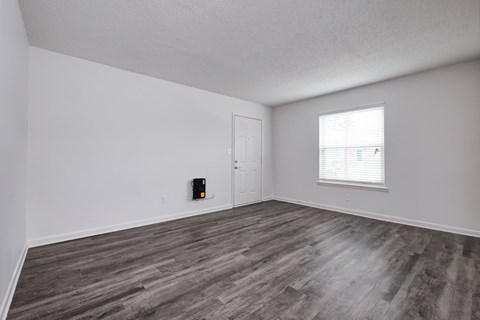 the living room of an apartment with wood flooring and a window