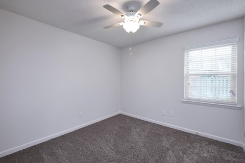 an empty bedroom with a ceiling fan and a window