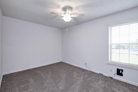 an empty bedroom with a ceiling fan and a window