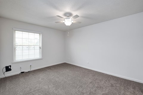 an empty bedroom with a ceiling fan and a window