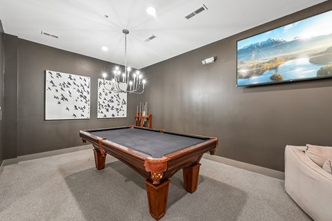 A pool table in a room with a painting on the wall and a couch.