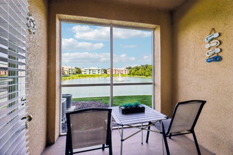 A patio with a table and chairs overlooking a pool and buildings.