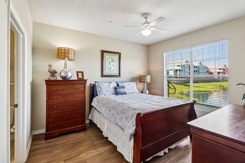 A bedroom with a bed, dresser, and window overlooking a lawn.