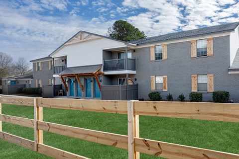 Building exterior view. A wooden fence in front of a grey building at Magnolia Apartments in Athens, Alabama