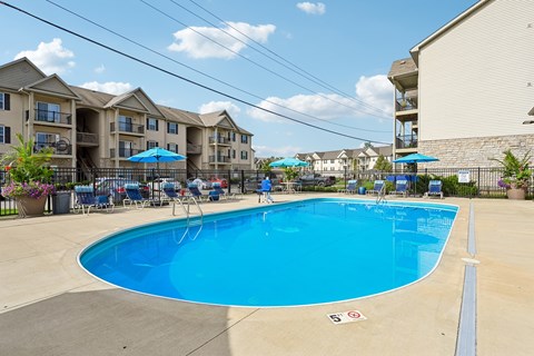 A swimming pool surrounded by chairs and umbrellas in front of apartment buildings.