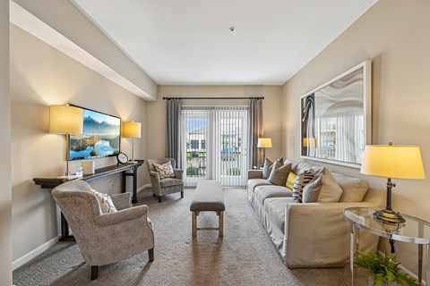 A well-lit, spacious living room with a grey sofa, a grey armchair, a grey coffee table, and a painting on the wall.