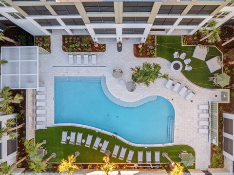 A large outdoor swimming pool surrounded by a white tile patio and lounge chairs.